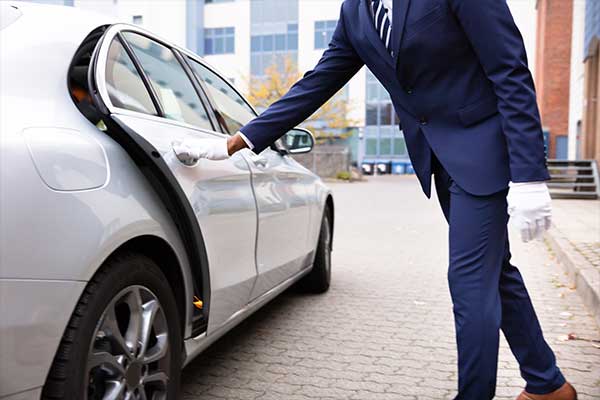 A man wearing a suit opening the gate of a car